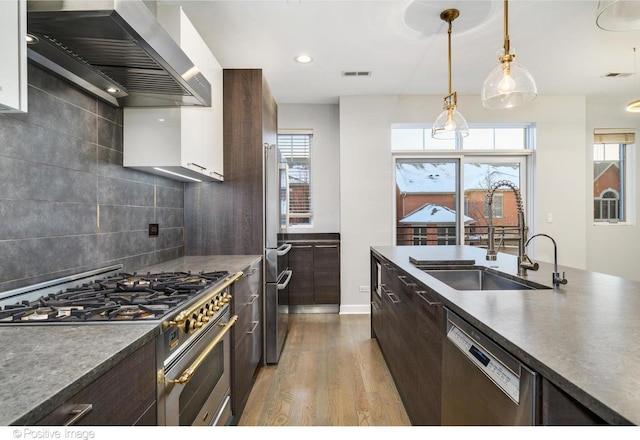 kitchen featuring appliances with stainless steel finishes, wall chimney range hood, decorative backsplash, and sink