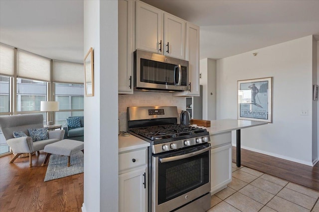 kitchen with appliances with stainless steel finishes, white cabinetry, light tile patterned flooring, and backsplash