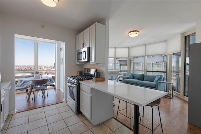 kitchen featuring stainless steel appliances, white cabinets, a kitchen breakfast bar, and light tile patterned floors