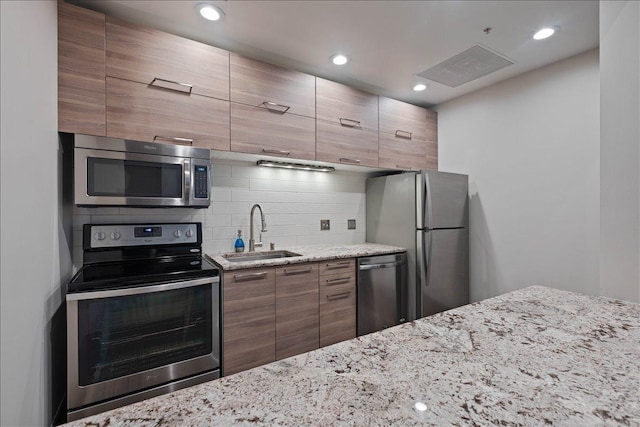 kitchen featuring light stone countertops, appliances with stainless steel finishes, backsplash, and sink