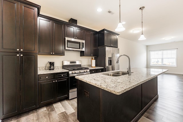 kitchen featuring appliances with stainless steel finishes, light hardwood / wood-style floors, sink, hanging light fixtures, and a center island with sink