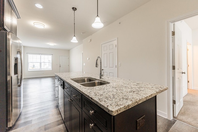 kitchen with a center island with sink, appliances with stainless steel finishes, hanging light fixtures, light hardwood / wood-style flooring, and sink