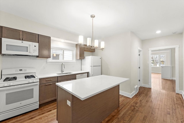 kitchen with white appliances, a center island, a notable chandelier, pendant lighting, and sink