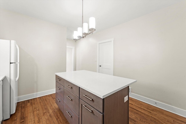 kitchen with white fridge, dark hardwood / wood-style floors, a kitchen island, a chandelier, and pendant lighting