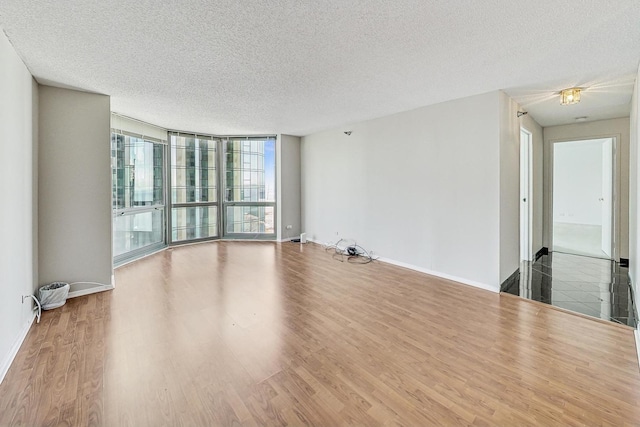 empty room with a wall of windows, wood-type flooring, and a textured ceiling