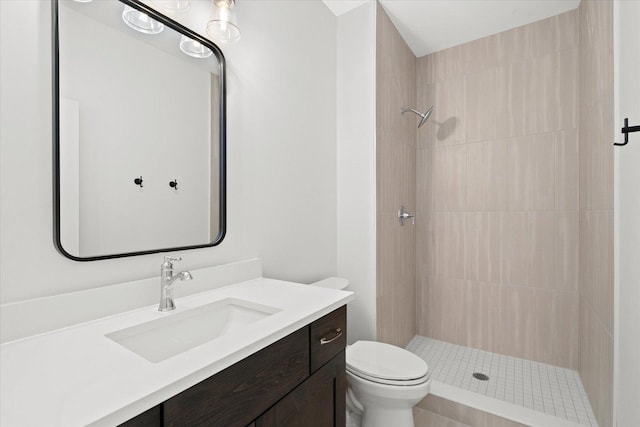 bathroom featuring toilet, tiled shower, and vanity