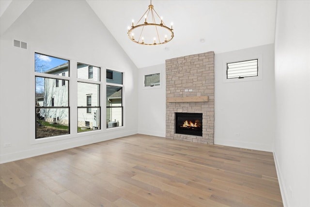 unfurnished living room with an inviting chandelier, high vaulted ceiling, light hardwood / wood-style floors, and a stone fireplace