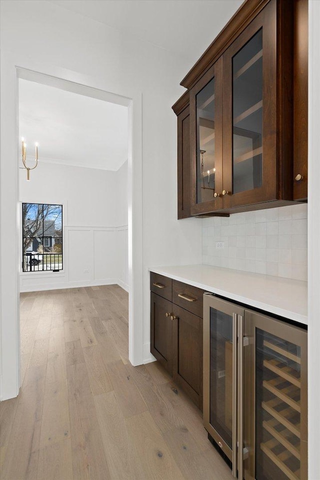 bar featuring decorative light fixtures, light wood-type flooring, wine cooler, backsplash, and dark brown cabinetry