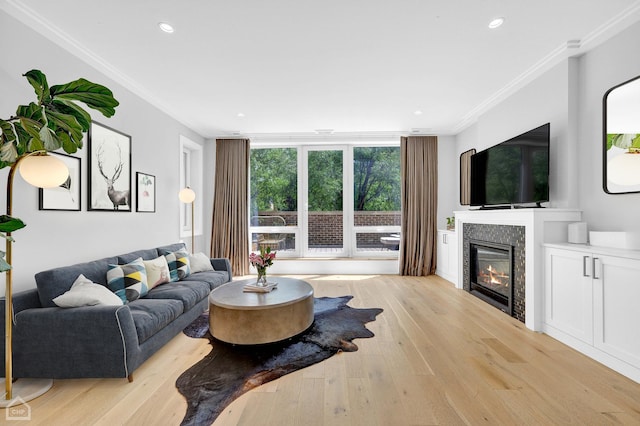 living room featuring a tiled fireplace, crown molding, light hardwood / wood-style floors, and a wall of windows