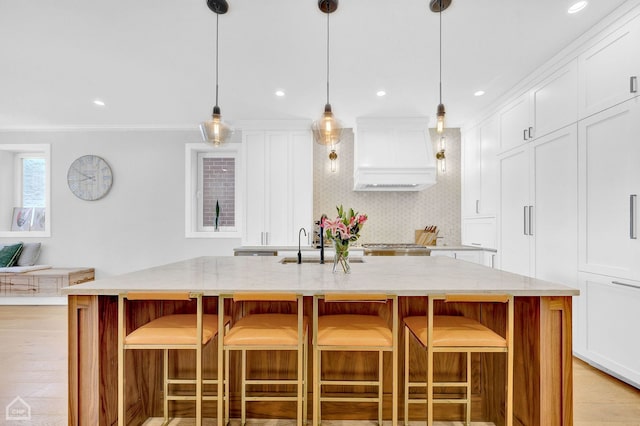 kitchen with a breakfast bar, custom range hood, and a center island with sink