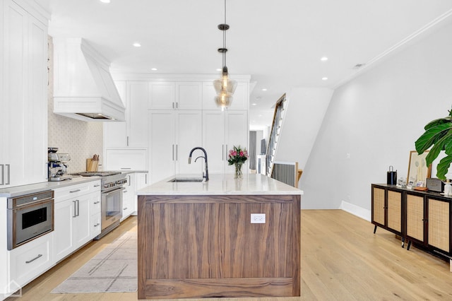 kitchen with sink, hanging light fixtures, high end stove, custom range hood, and an island with sink