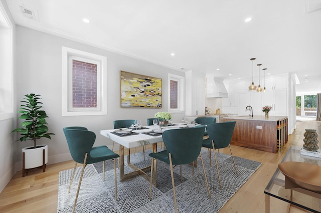 dining room with sink, light hardwood / wood-style flooring, and ornamental molding