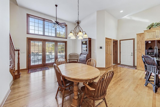 dining area with a high ceiling, ceiling fan with notable chandelier, light wood-type flooring, and french doors