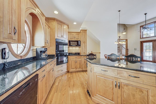 kitchen featuring light brown cabinetry, light hardwood / wood-style flooring, dark stone countertops, hanging light fixtures, and black appliances