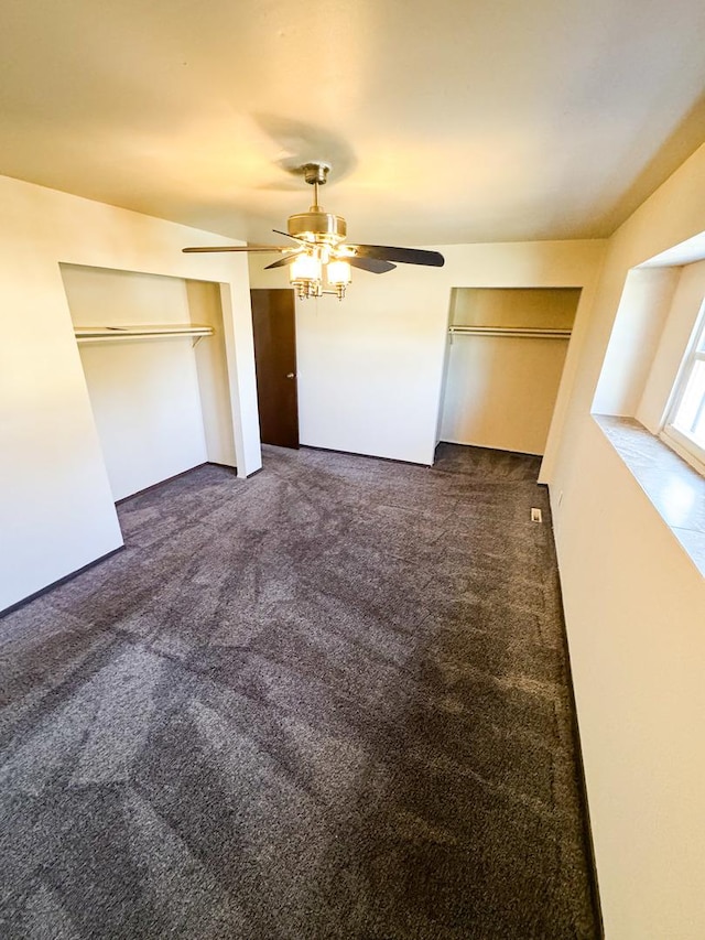 unfurnished bedroom featuring ceiling fan, multiple closets, and dark carpet