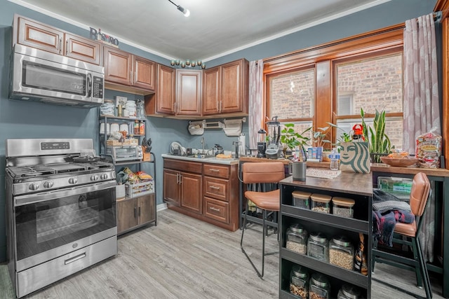 kitchen with sink, ornamental molding, stainless steel appliances, and light hardwood / wood-style floors