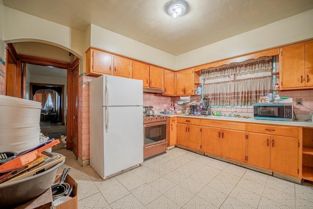 kitchen with stove, backsplash, sink, and white fridge