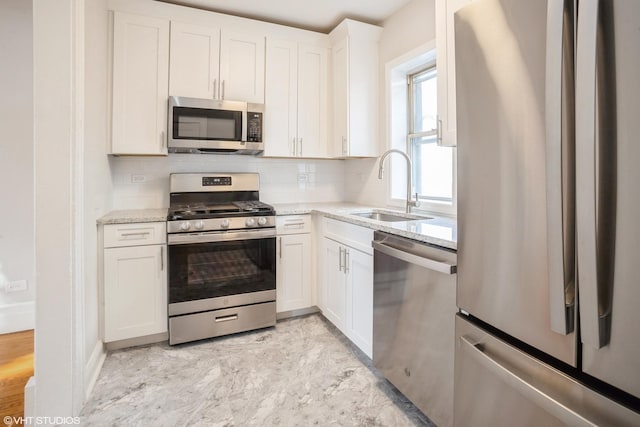 kitchen with backsplash, sink, stainless steel appliances, white cabinets, and light stone counters