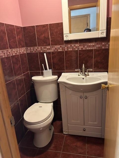 bathroom with tile walls, toilet, vanity, and tile patterned flooring