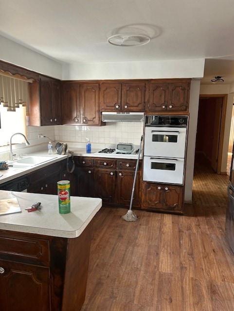 kitchen with backsplash, dark brown cabinets, sink, white appliances, and dark hardwood / wood-style flooring