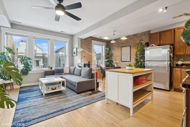 kitchen with butcher block countertops, stainless steel refrigerator, ceiling fan, light hardwood / wood-style floors, and brick wall