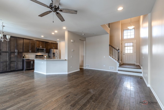 unfurnished living room featuring ceiling fan with notable chandelier, a high ceiling, and dark wood-type flooring