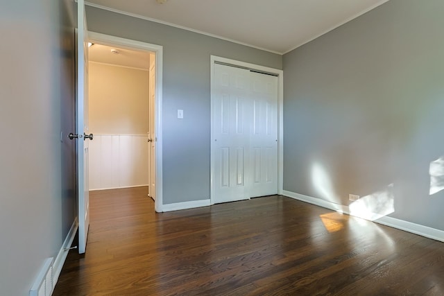 unfurnished bedroom featuring dark wood-type flooring, a closet, and crown molding