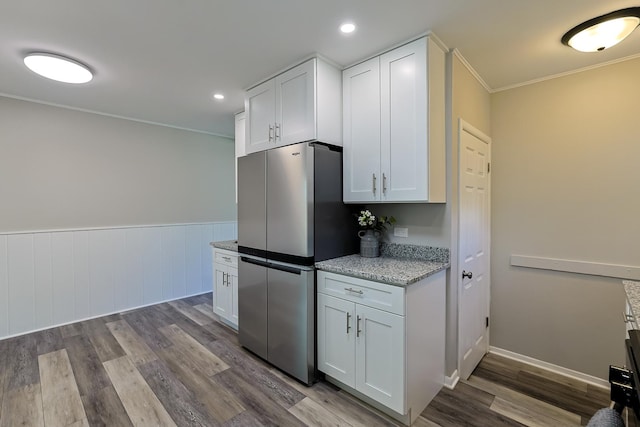 kitchen featuring light stone counters, light wood-type flooring, crown molding, white cabinetry, and stainless steel refrigerator