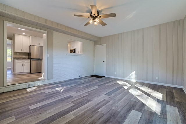 unfurnished living room featuring brick wall, ceiling fan, and light hardwood / wood-style flooring