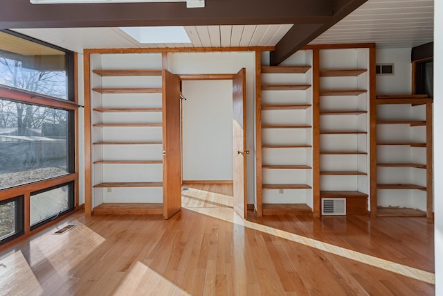 additional living space featuring beamed ceiling, light wood-type flooring, and a skylight