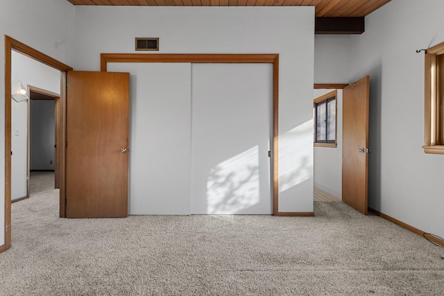 unfurnished bedroom featuring beamed ceiling, light carpet, wooden ceiling, and a closet