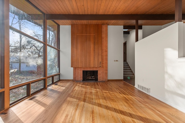 unfurnished living room featuring floor to ceiling windows, a brick fireplace, a healthy amount of sunlight, and light hardwood / wood-style flooring