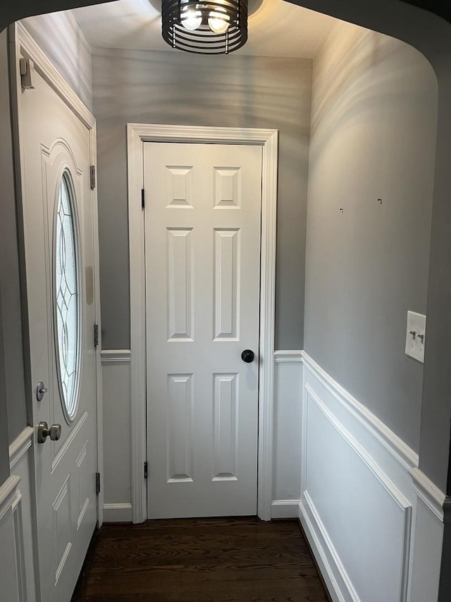 entrance foyer with dark wood-type flooring, arched walkways, wainscoting, and a decorative wall