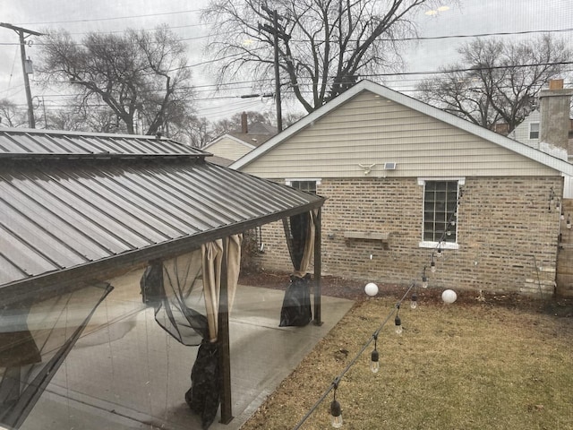 view of property exterior with metal roof, brick siding, and a patio area