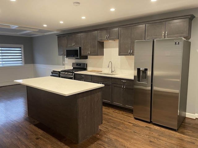 kitchen featuring light countertops, appliances with stainless steel finishes, dark wood-type flooring, a sink, and a kitchen island