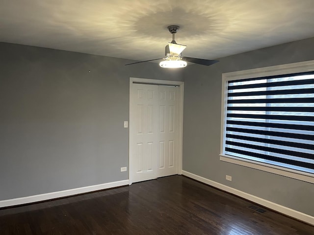 empty room featuring ceiling fan, dark wood-type flooring, visible vents, and baseboards