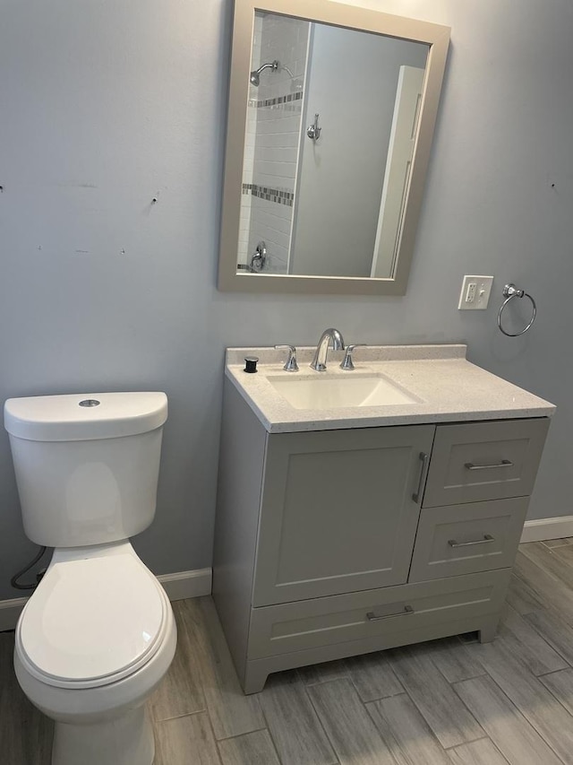 bathroom featuring baseboards, vanity, toilet, and tiled shower