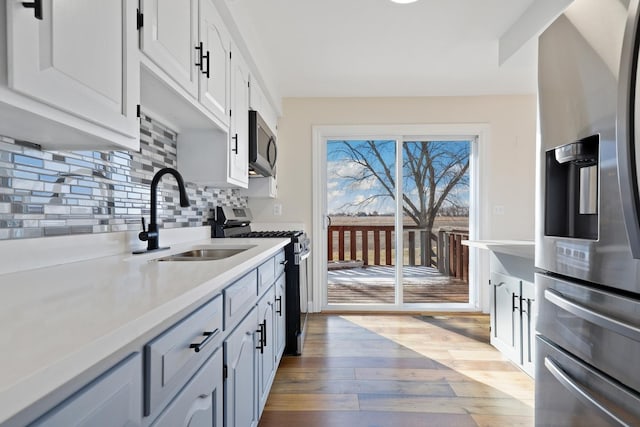 kitchen with light hardwood / wood-style floors, appliances with stainless steel finishes, white cabinetry, sink, and backsplash