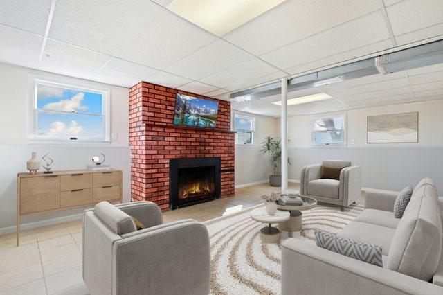 living room with a drop ceiling, light tile patterned floors, and a brick fireplace