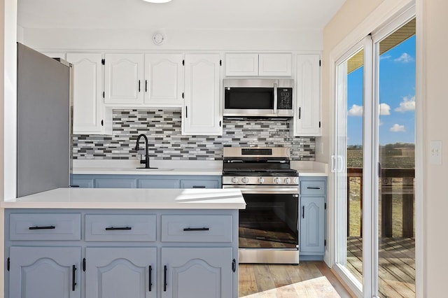 kitchen featuring white cabinets, appliances with stainless steel finishes, decorative backsplash, sink, and light hardwood / wood-style flooring