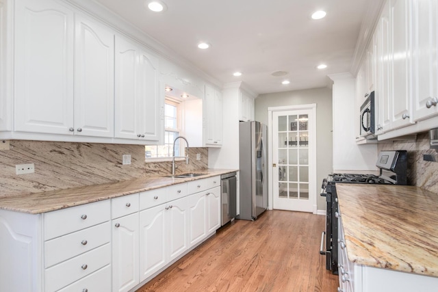 kitchen featuring appliances with stainless steel finishes, white cabinets, light stone counters, and sink