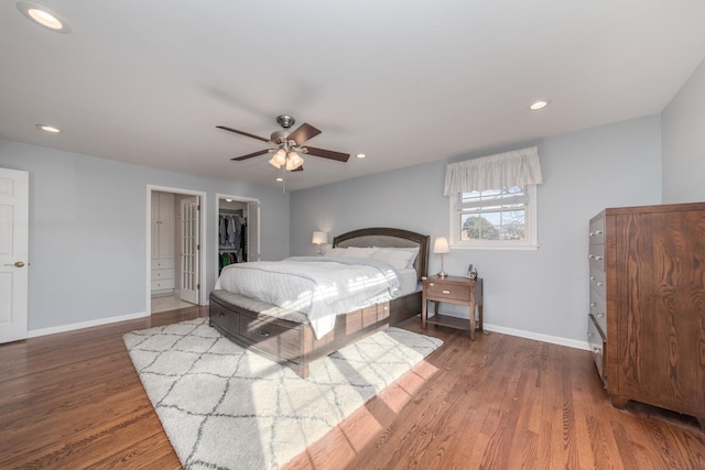 bedroom with dark wood-type flooring, ceiling fan, a walk in closet, and a closet