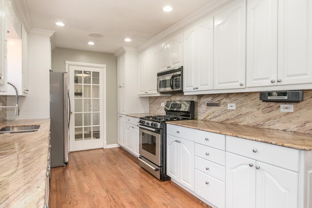 kitchen with stainless steel appliances, decorative backsplash, white cabinets, and light stone counters