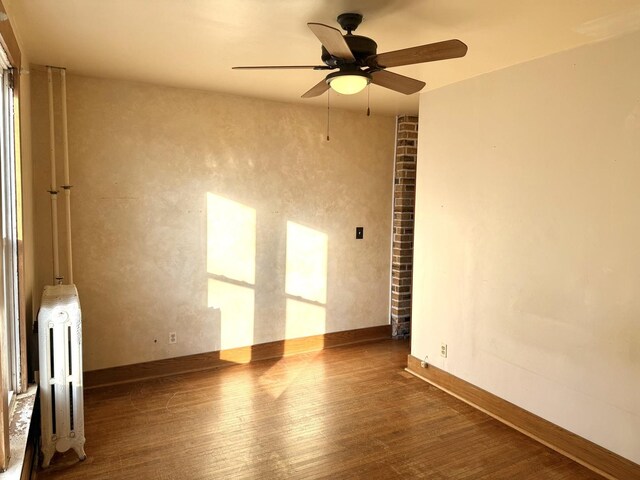 empty room featuring radiator, ceiling fan, and dark hardwood / wood-style flooring