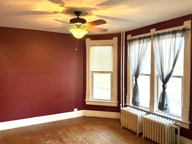 unfurnished room featuring ceiling fan, radiator, wood-type flooring, and a wealth of natural light