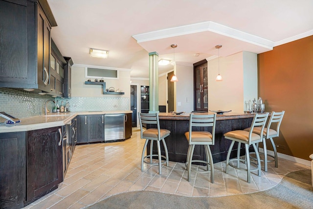 kitchen with pendant lighting, tasteful backsplash, sink, ornamental molding, and a breakfast bar area