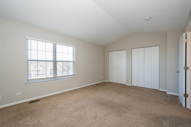 unfurnished bedroom featuring lofted ceiling, two closets, and light carpet