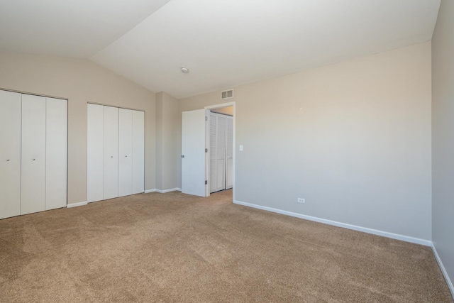 unfurnished bedroom featuring two closets, vaulted ceiling, and light carpet