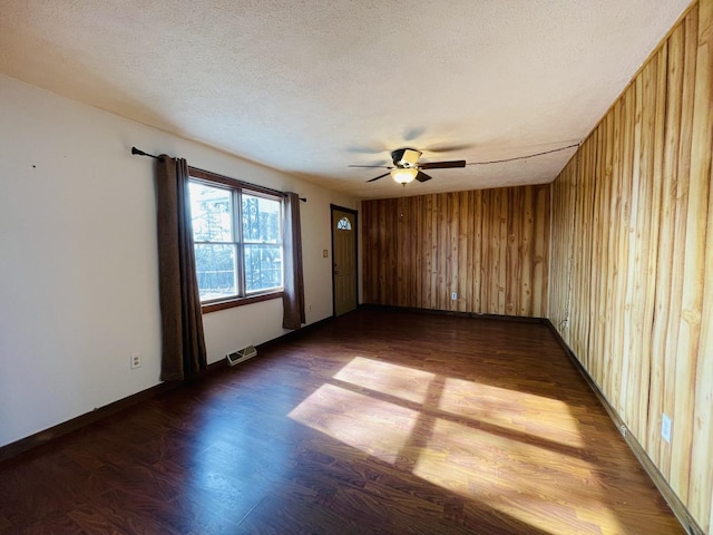 empty room featuring dark wood-type flooring, a textured ceiling, ceiling fan, and wood walls