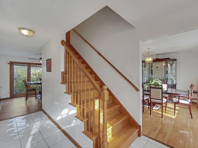 staircase with ceiling fan with notable chandelier and tile patterned flooring